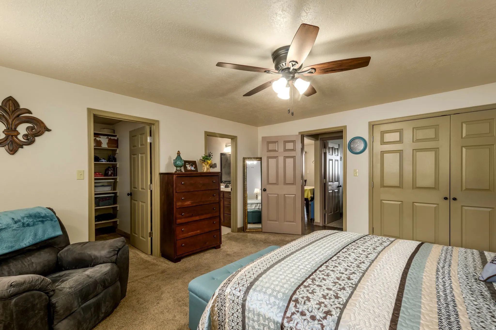 Bedroom with carpet, a textured ceiling, ceiling fan, ensuite bathroom, and a spacious closet