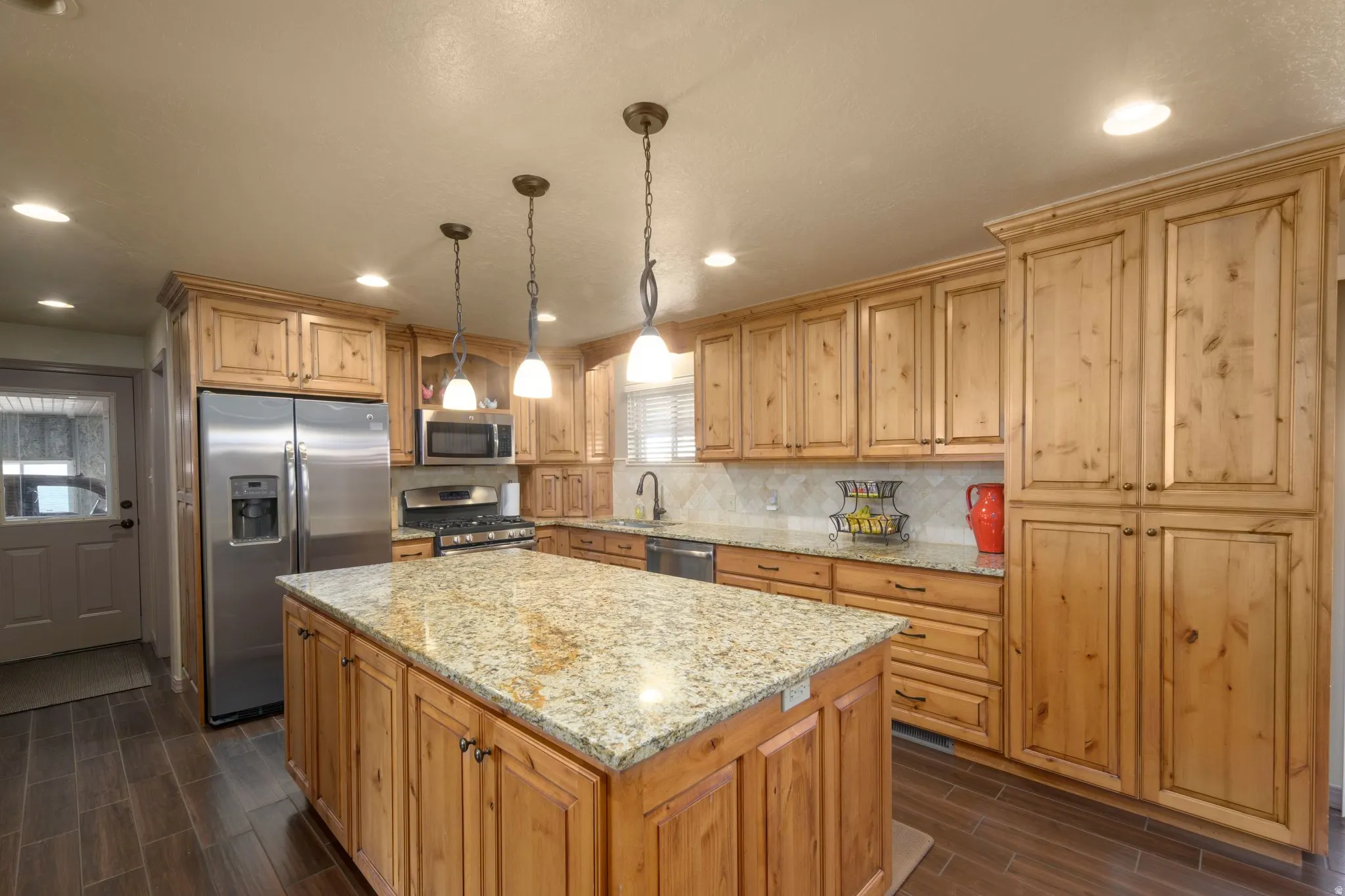 Kitchen featuring stainless steel appliances, light stone countertops, hanging light fixtures, a center island, and wood tiled floors