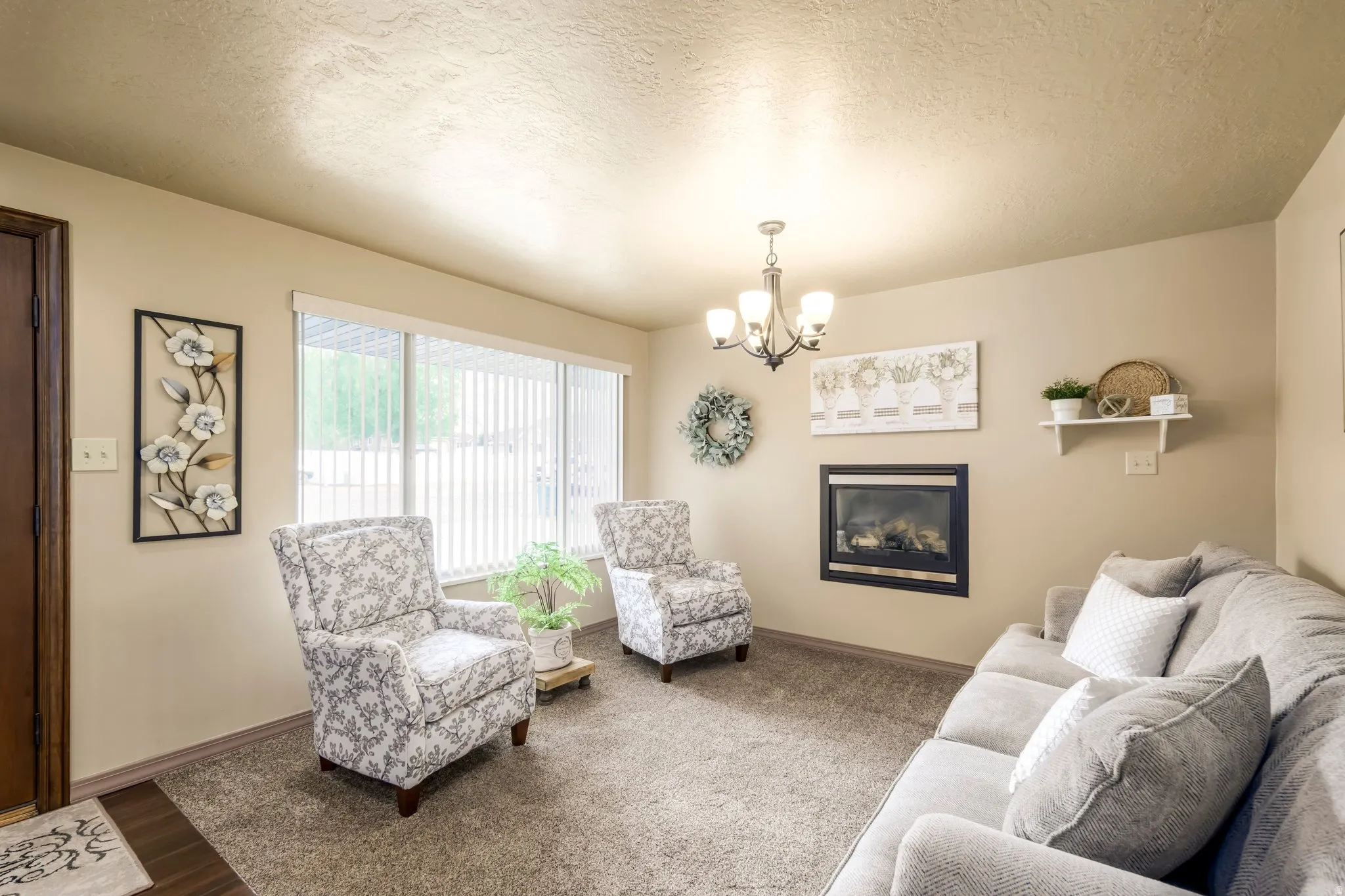 Living area with a textured ceiling, a chandelier, wood finished floors, and a glass covered fireplace