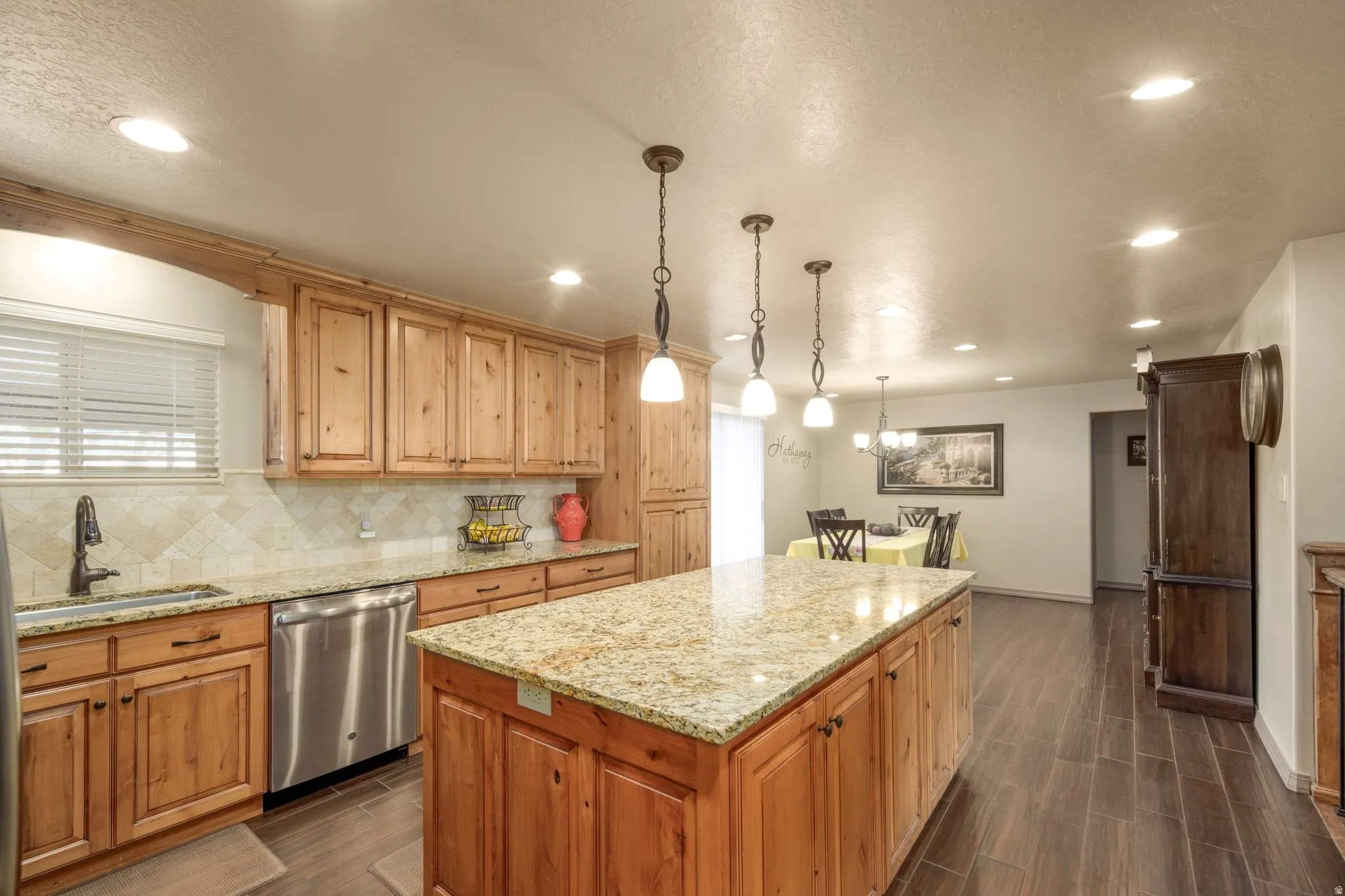 Kitchen with dishwasher, backsplash, a kitchen island, light stone countertops, and wood tiled floors