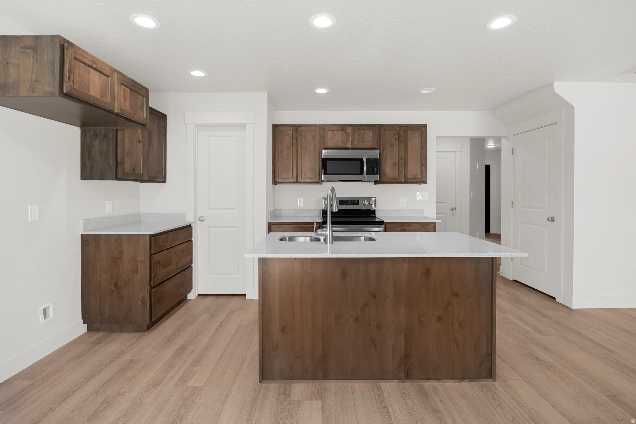 Kitchen featuring stainless steel appliances, light wood-type flooring, an island with sink, light stone countertops, and recessed lighting
