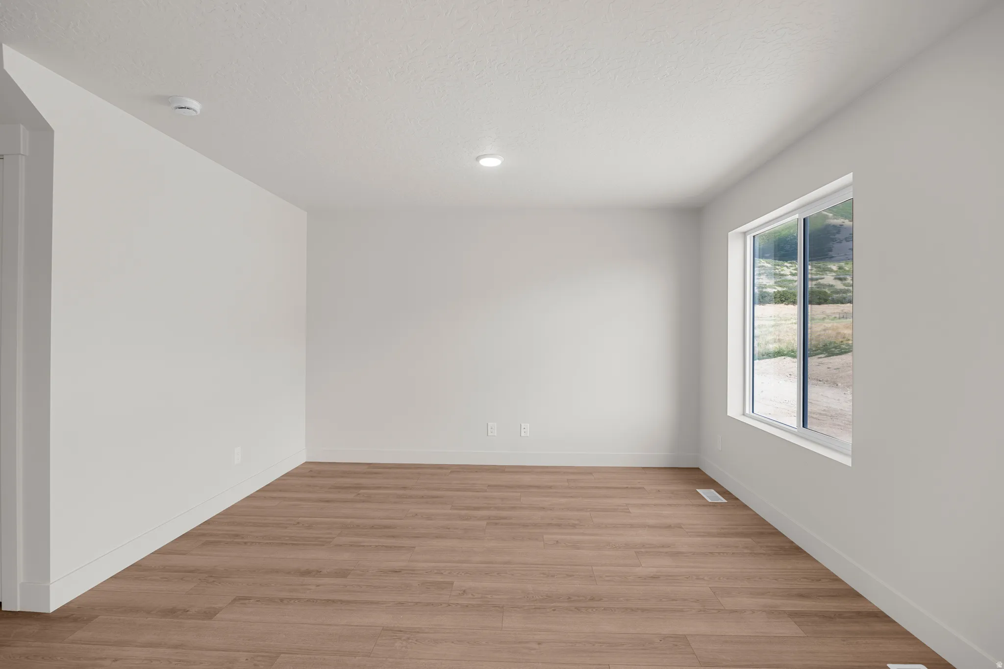 Spare room featuring light wood-type flooring and a textured ceiling