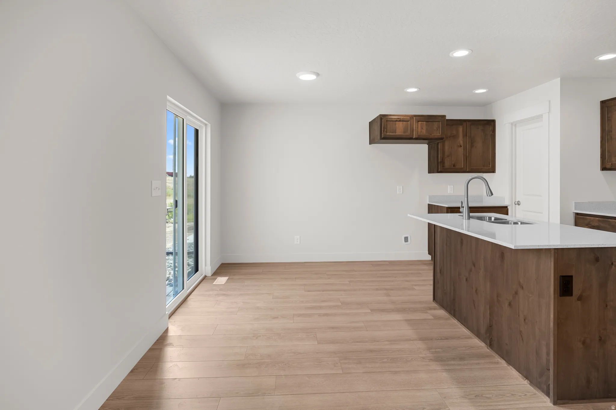 Kitchen with light wood-style floors, recessed lighting, light stone countertops, a center island with sink, and dark wood finish cabinets