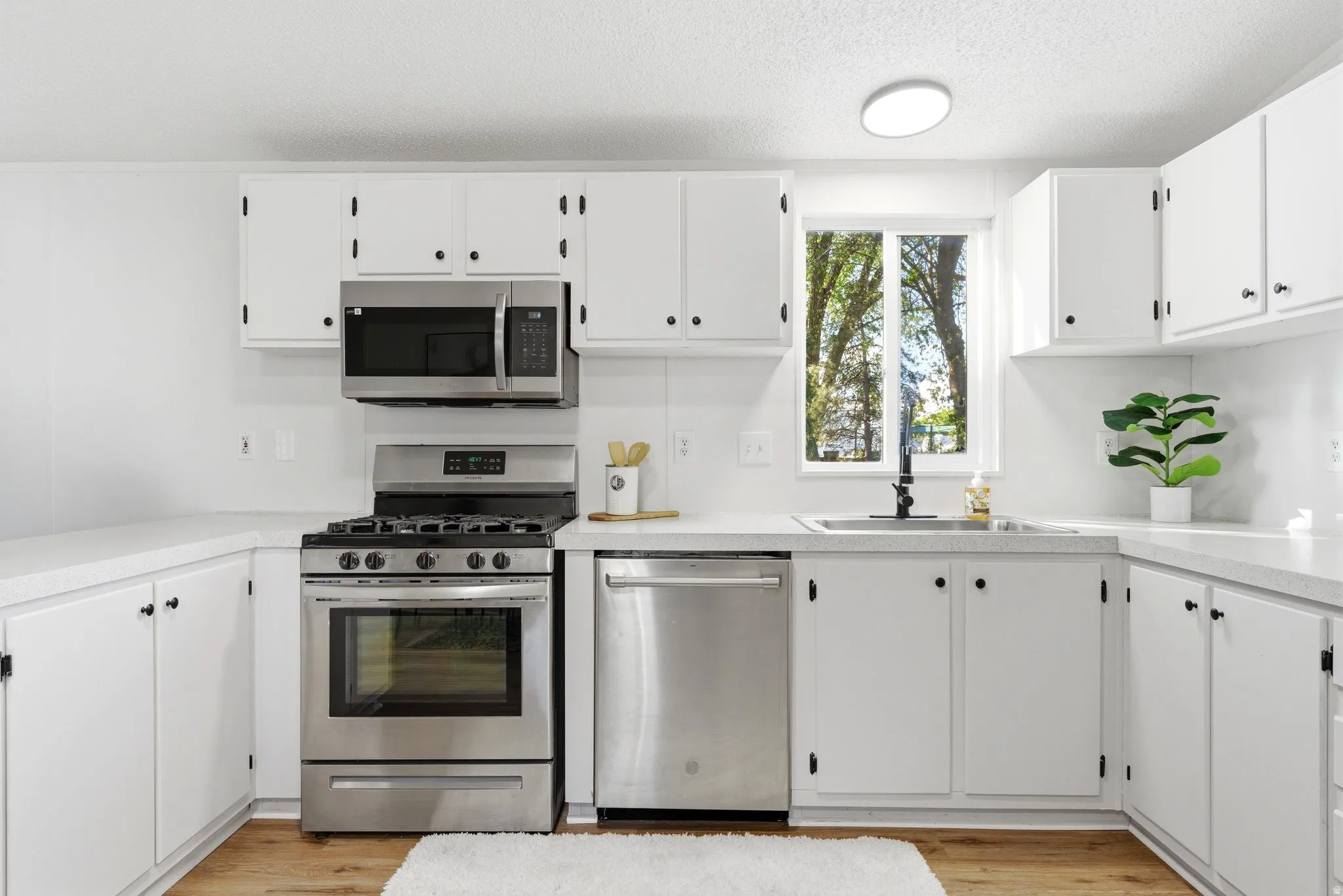 Kitchen featuring stainless steel appliances, light countertops, white cabinets, a textured ceiling, and light wood-style flooring