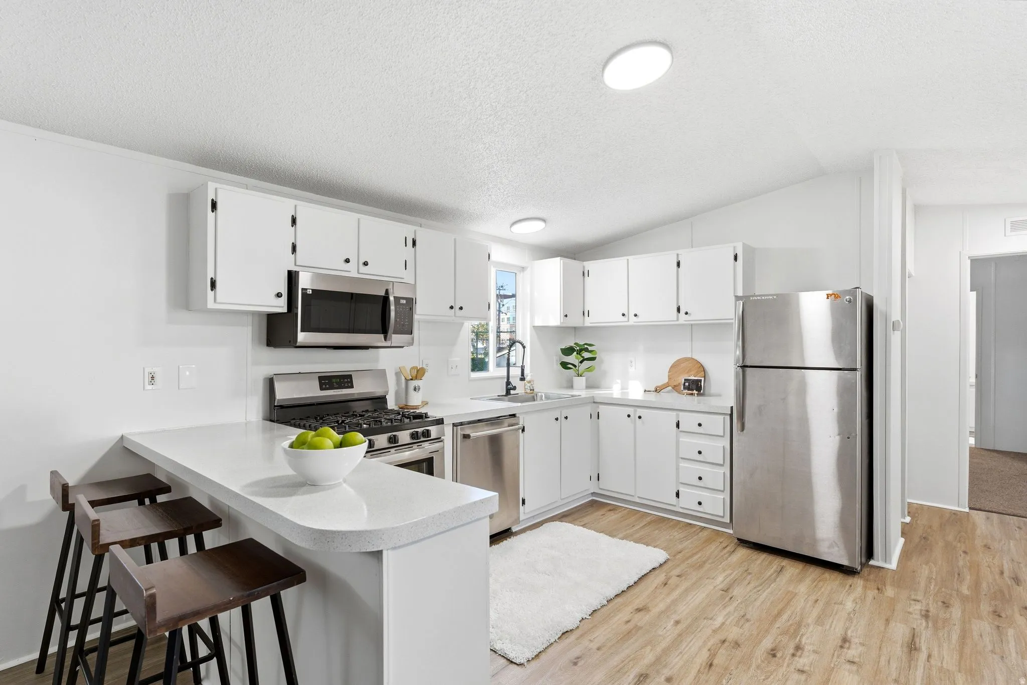 Kitchen with light countertops, white cabinetry, stainless steel appliances, and a breakfast bar
