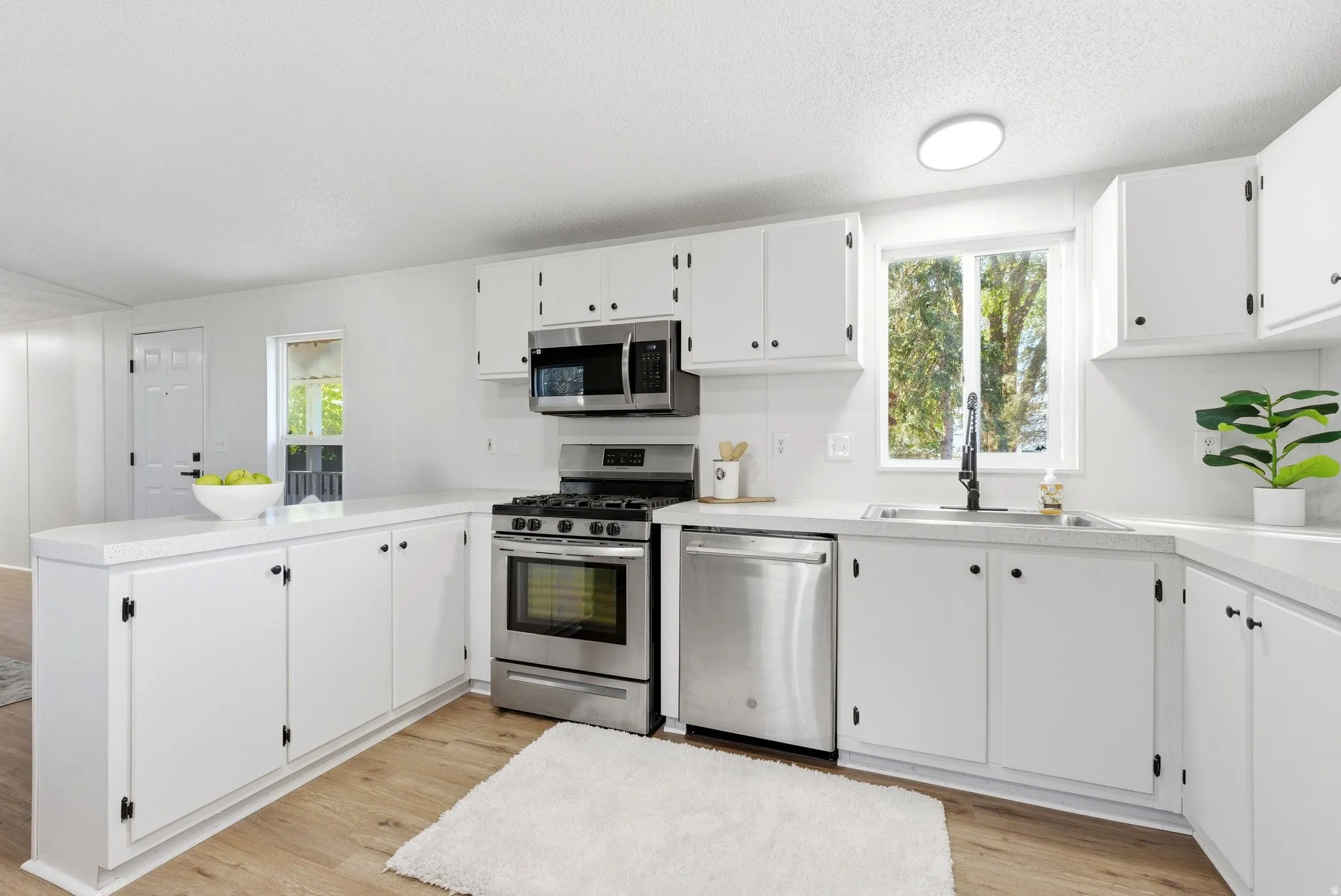 Kitchen featuring a peninsula, stainless steel appliances, light countertops, white cabinetry, and a textured ceiling