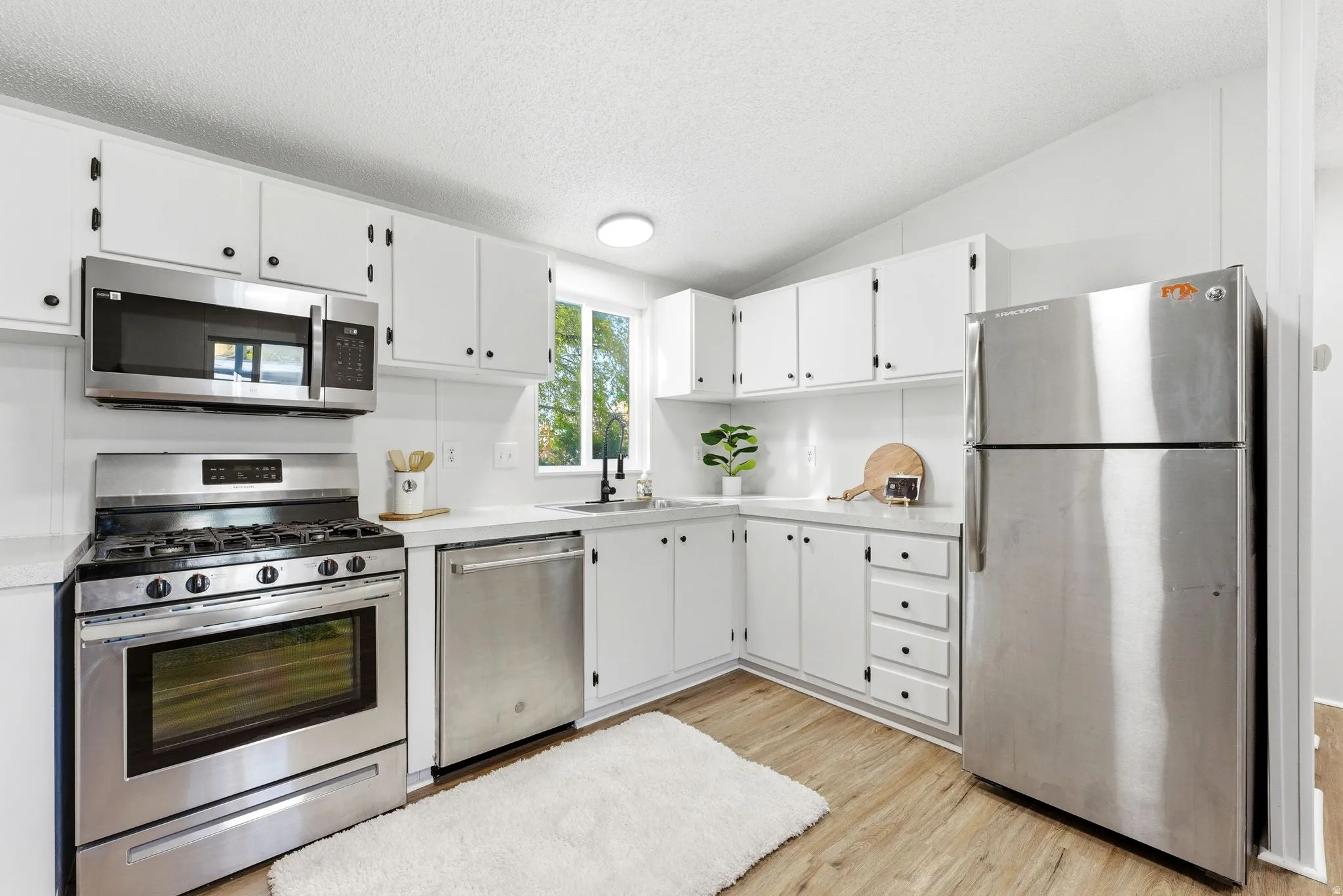 Kitchen featuring stainless steel appliances, light countertops, white cabinetry, and light wood-style flooring