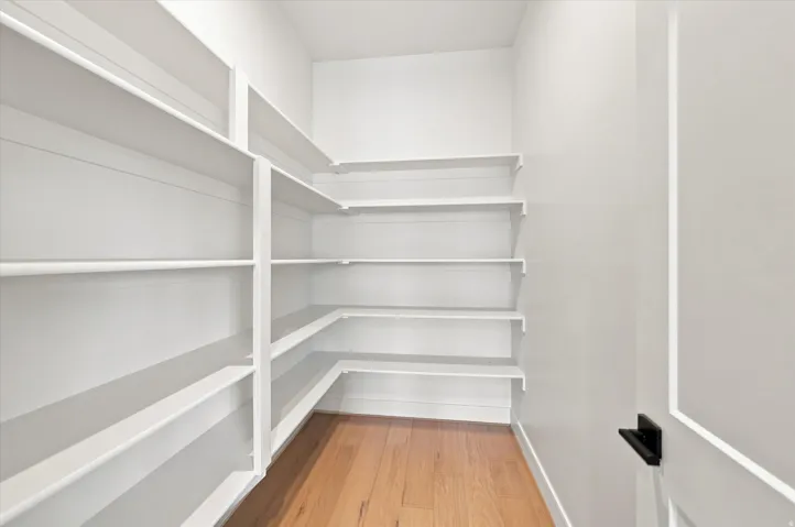 Expansive pantry featuring extensive built-in shelving, durable wood-finish flooring, and crisp white walls