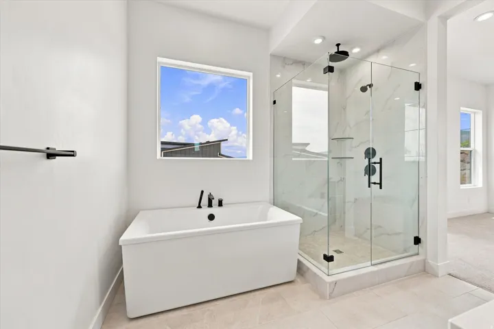 Freestanding tub with matte black fixtures, separate glass-enclosed shower with tile surround, and tiled flooring
