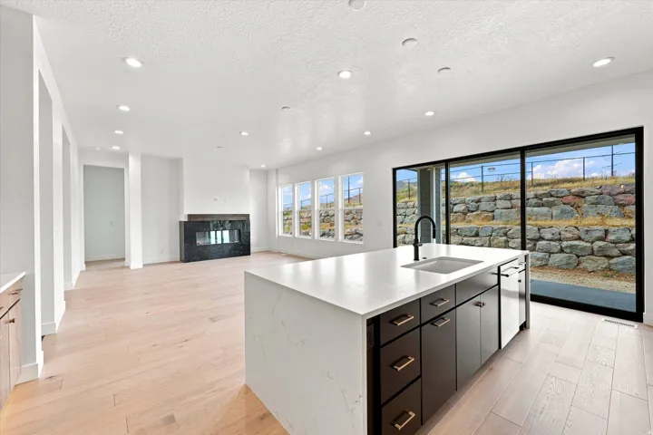 Spacious open-concept living area featuring light wood-finish flooring, a modern black fireplace, and a kitchen island with a built-in sink