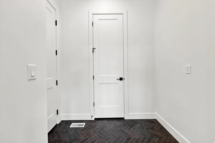 Herringbone pattern wood-finish flooring, white panel doors with matte black hardware, and crisp white walls