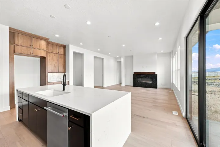 Open-concept living space with light wood-finish flooring, a contemporary fireplace with a dark stone surround, a kitchen island with a white solid surface countertop and undermount sink, and a full wall of glass sliders