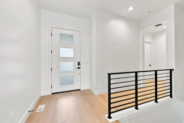 Entryway featuring a contemporary front door with frosted glass panels, wood-finish flooring, recessed lighting, and a modern horizontal bar railing