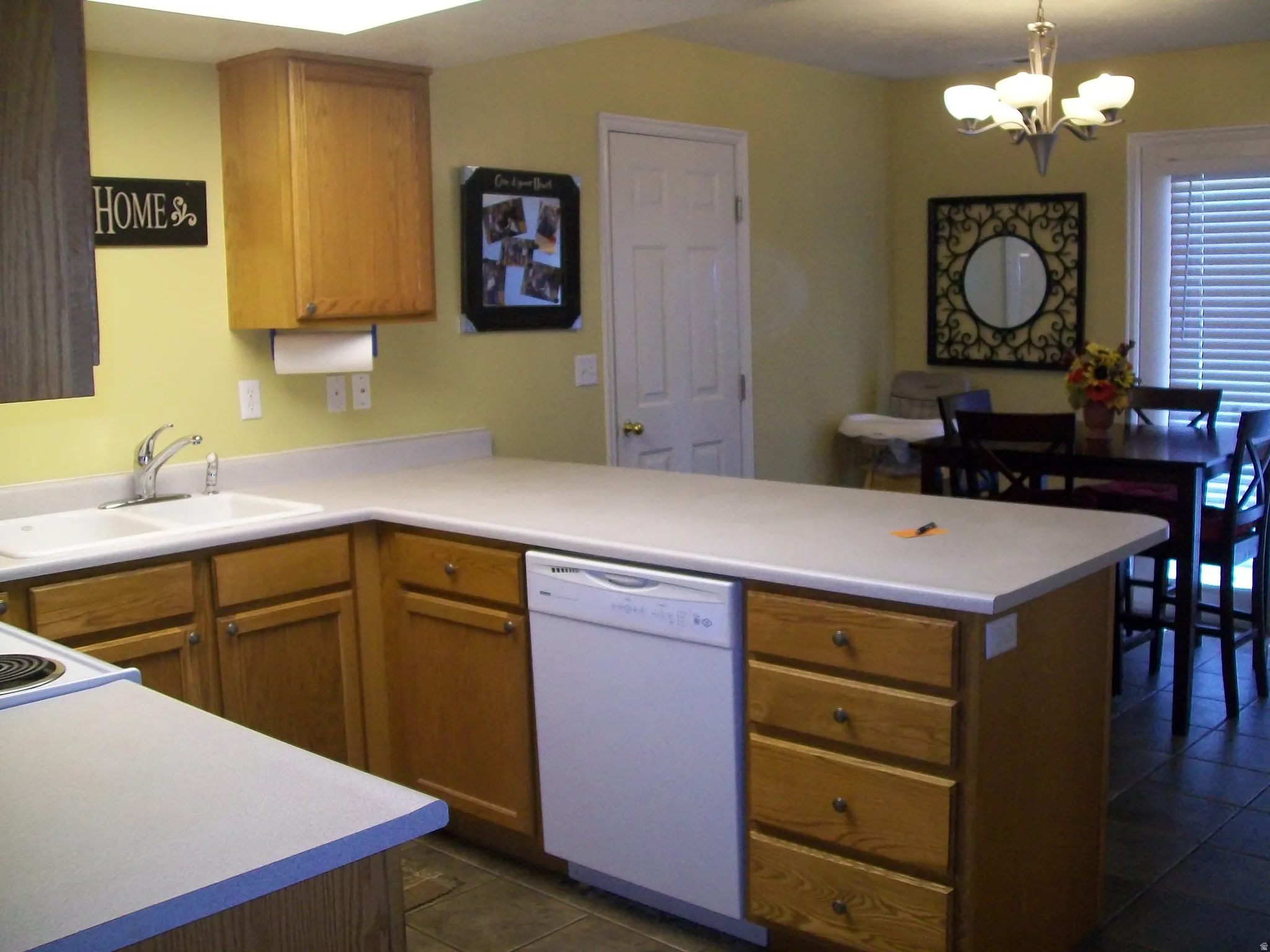 Kitchen featuring a peninsula, wood finish cabinetry, dishwasher, dark tile patterned flooring, and suspended lighting