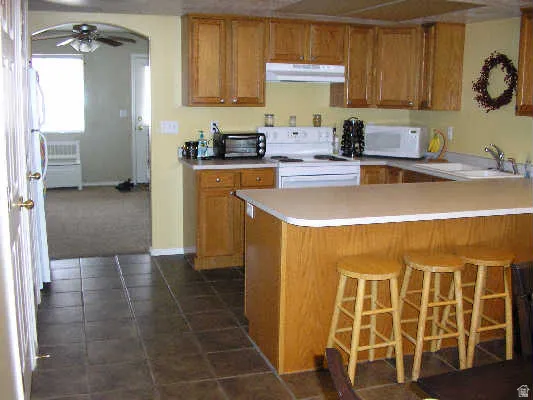 Kitchen featuring wood finish cabinets, a ceiling fan, light countertops, and white appliances