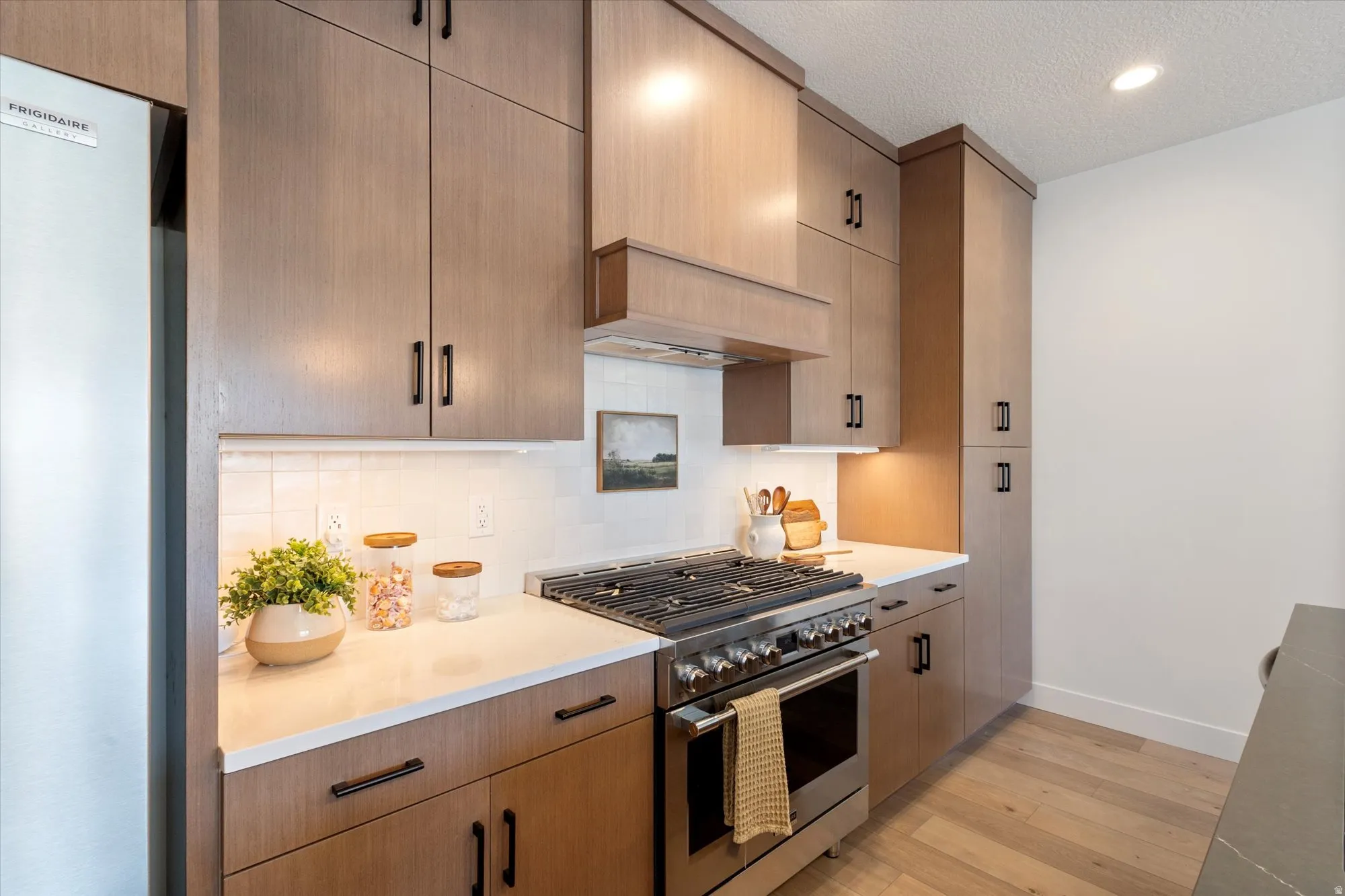 Kitchen with stainless steel gas range, light wood finished floors, freestanding refrigerator, a textured ceiling, and tasteful backsplash