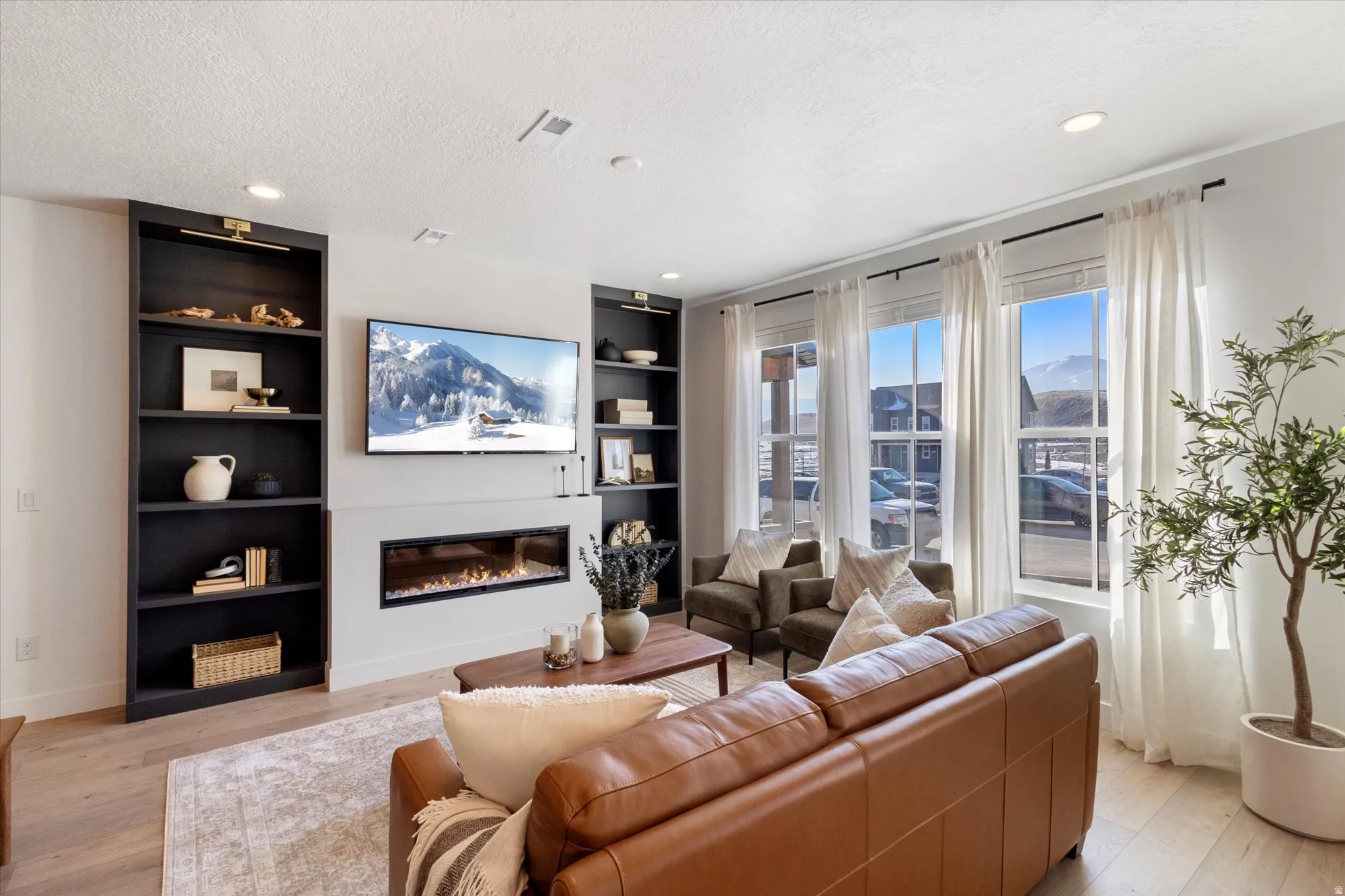 Living room featuring light wood-type flooring, a glass covered fireplace, built in shelves, recessed lighting, and a textured ceiling