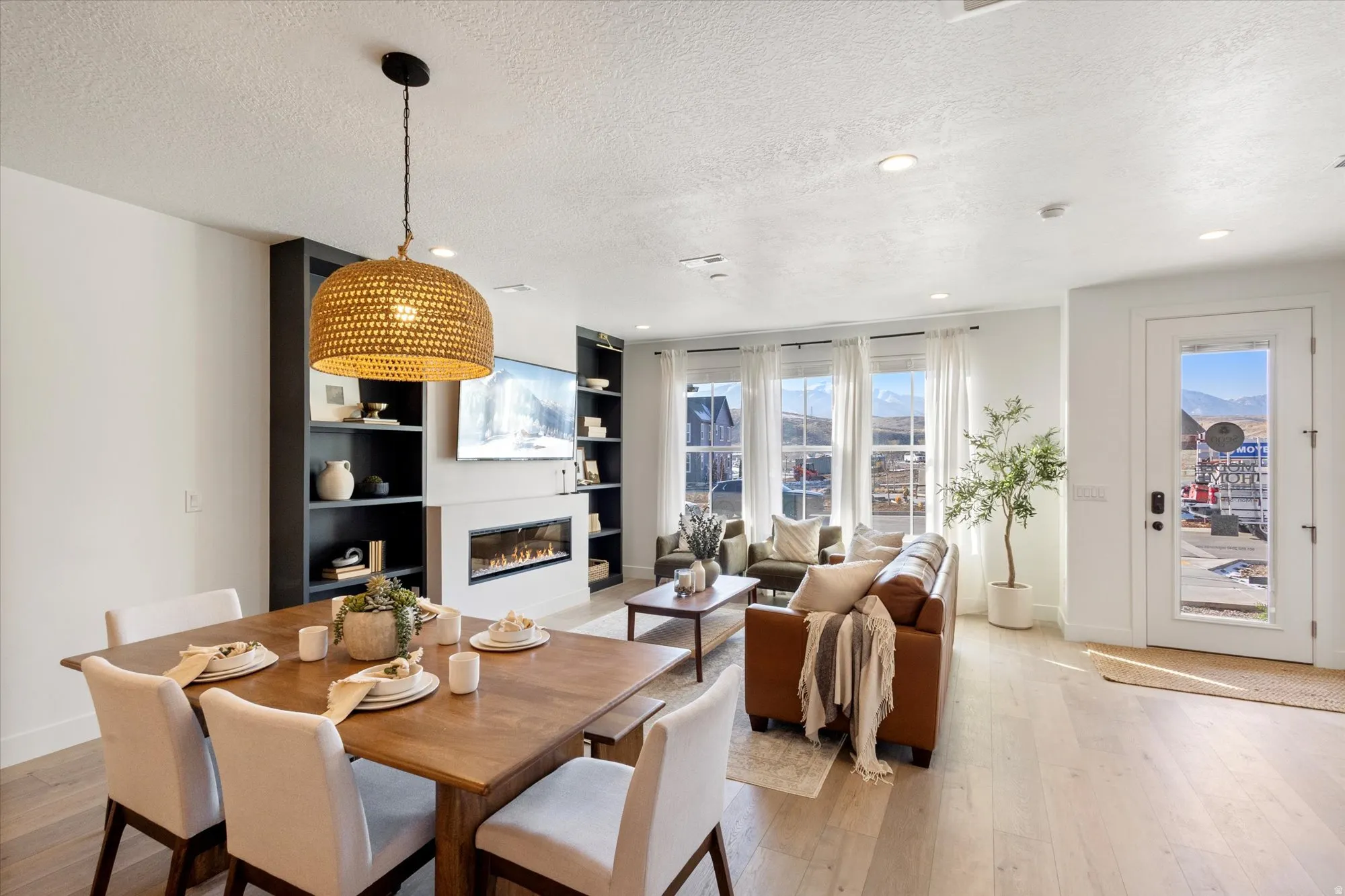 Dining area featuring light wood-style floors, a textured ceiling, a glass covered fireplace, recessed lighting, and built in shelves