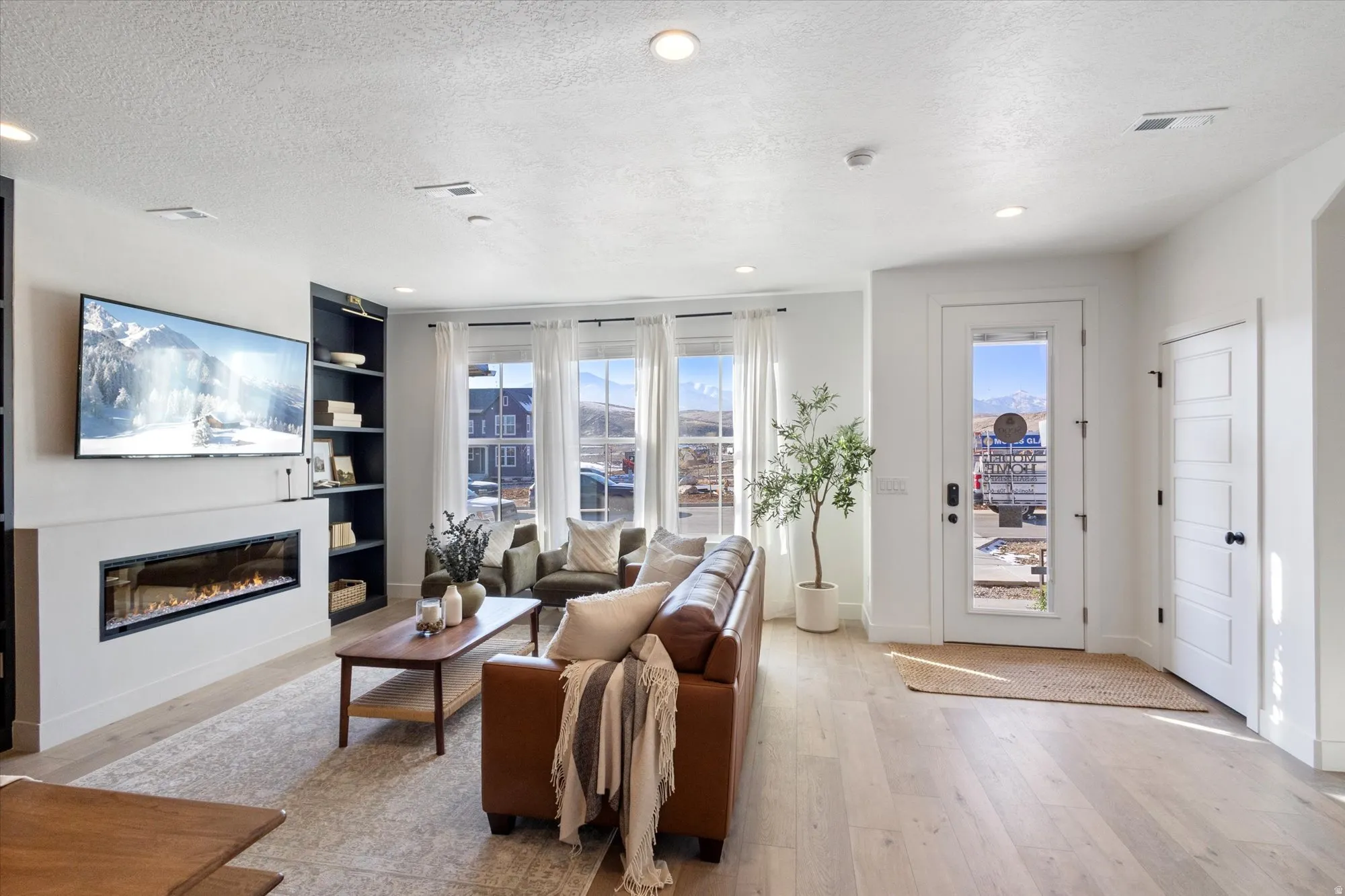 Living room with a textured ceiling, light wood finished floors, a glass covered fireplace, built in features, and recessed lighting