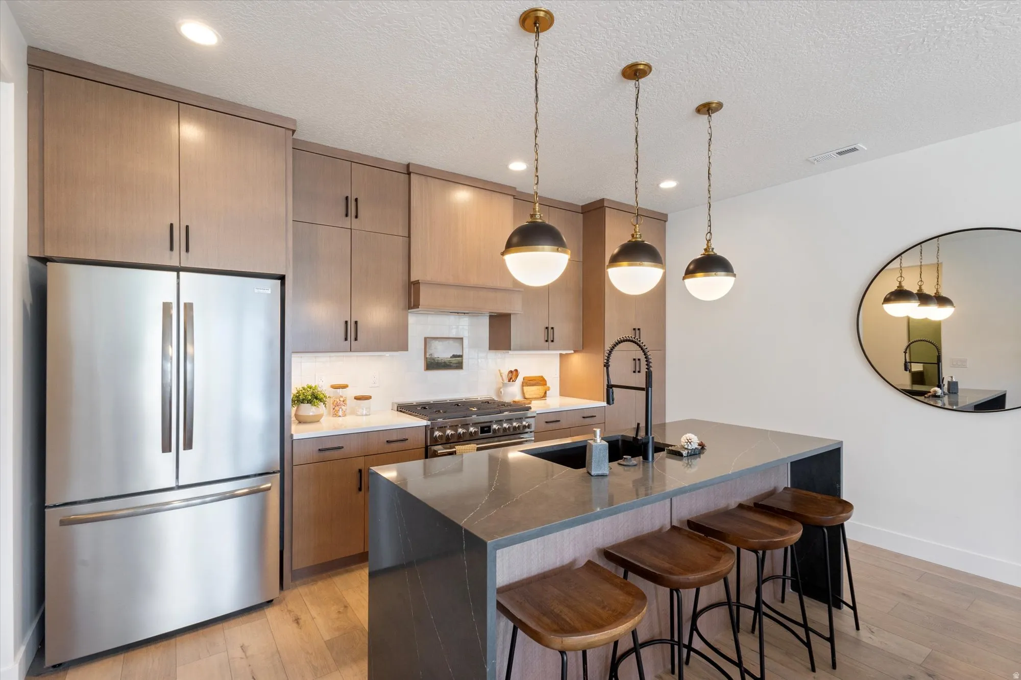 Kitchen with stainless steel appliances, dark stone counters, a kitchen bar, light wood finished floors, and a textured ceiling