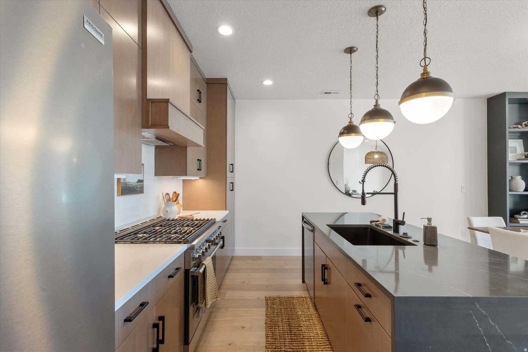 Two tone kitchen featuring stainless steel appliances, dark stone counters, light wood-type flooring, hanging light fixtures, and a large island with sink