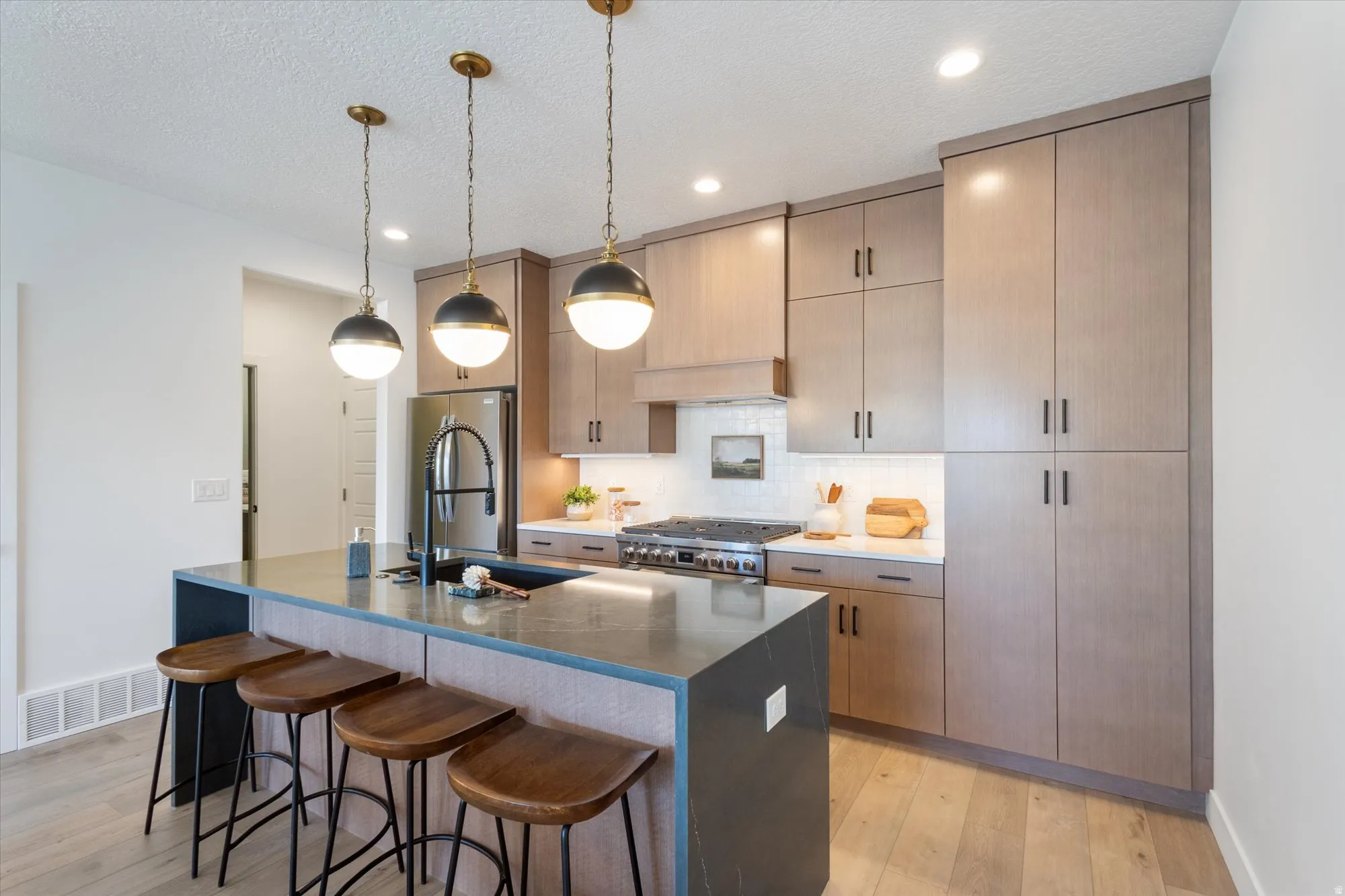 Kitchen featuring light wood-style flooring, a breakfast bar, backsplash, dark stone counters, and decorative light fixtures