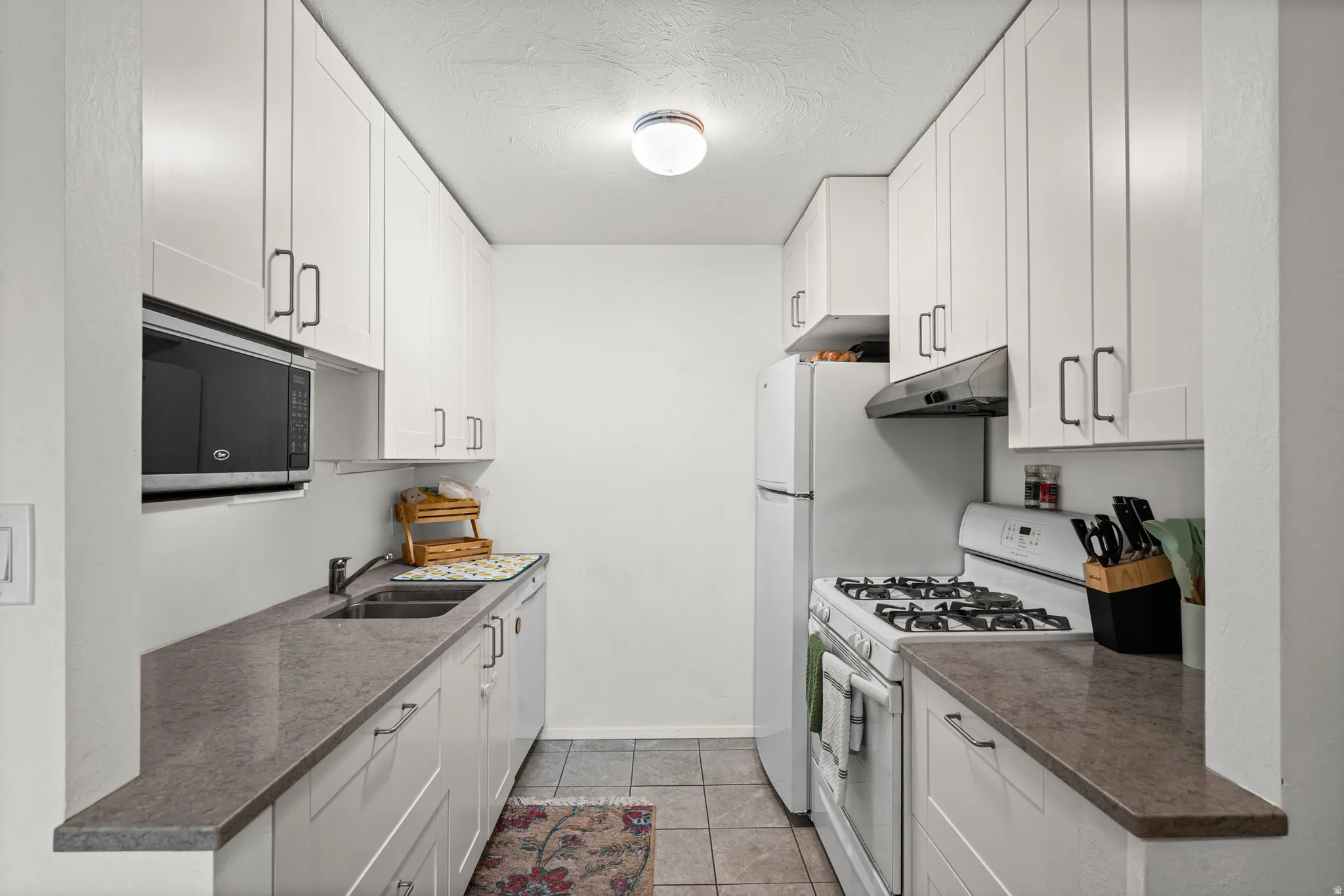 Kitchen featuring white cabinetry, white appliances, light tile patterned flooring, a textured ceiling, and dark quartz counters