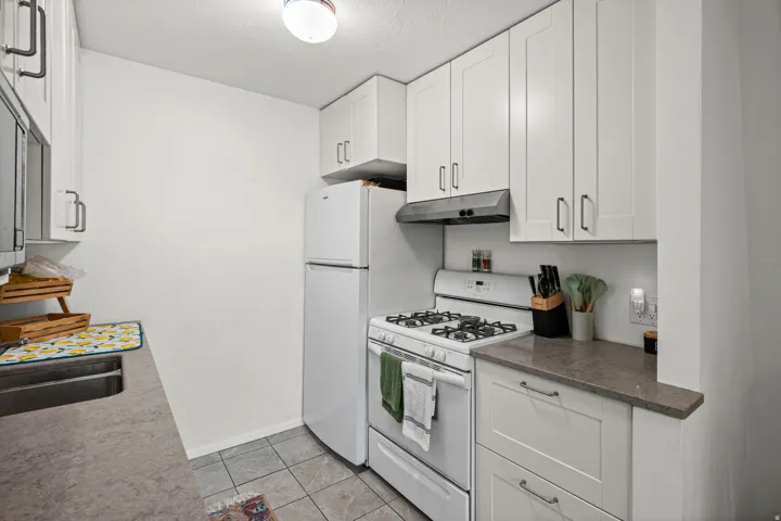 Kitchen featuring white gas stove, white cabinetry, and light tile patterned floors