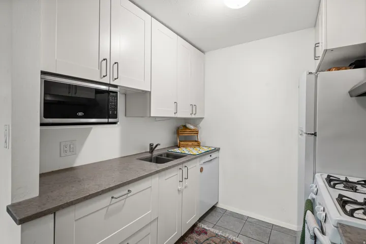 Kitchen featuring stainless steel microwave, white cabinetry, tile patterned floors, and white dishwasher