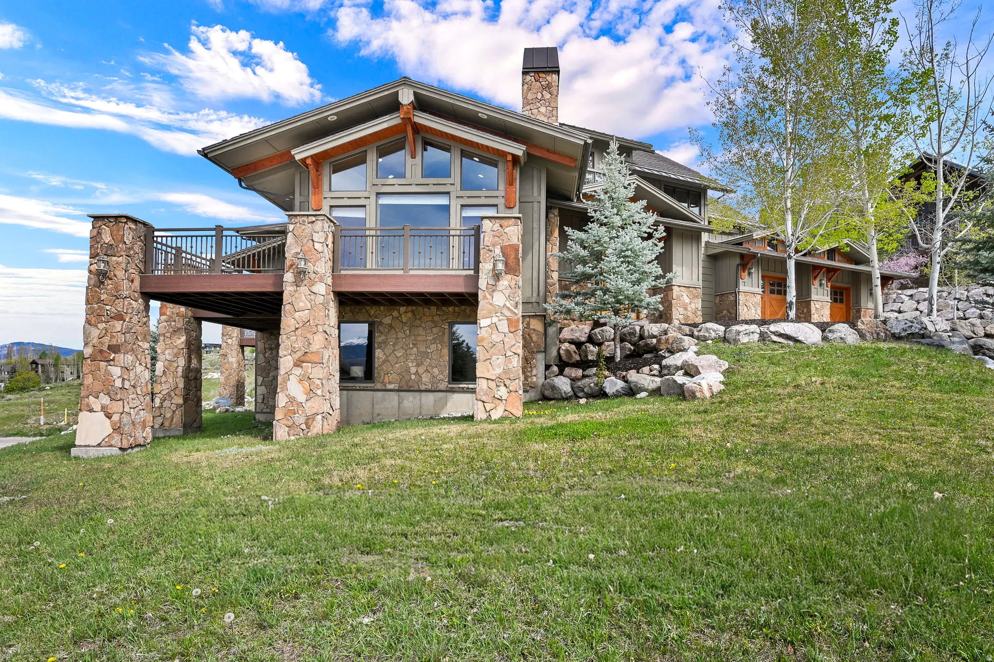 Back of house featuring stone siding, a chimney, a yard, and a wooden deck