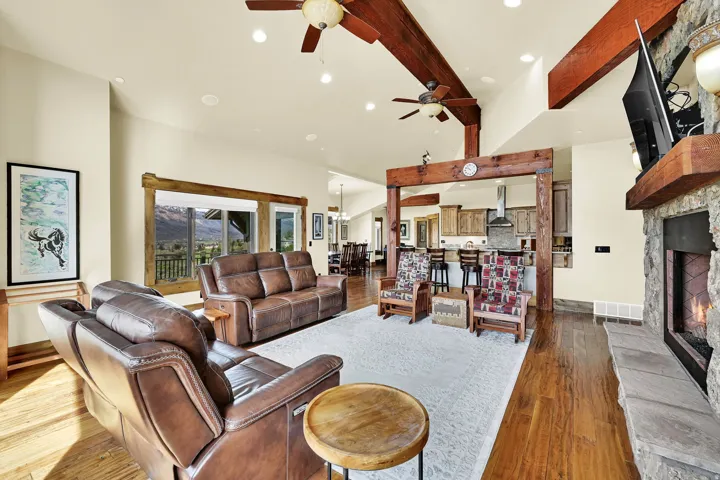 Living room with a fireplace, dark wood finished floors, beamed ceiling, a ceiling fan, and hanging lights