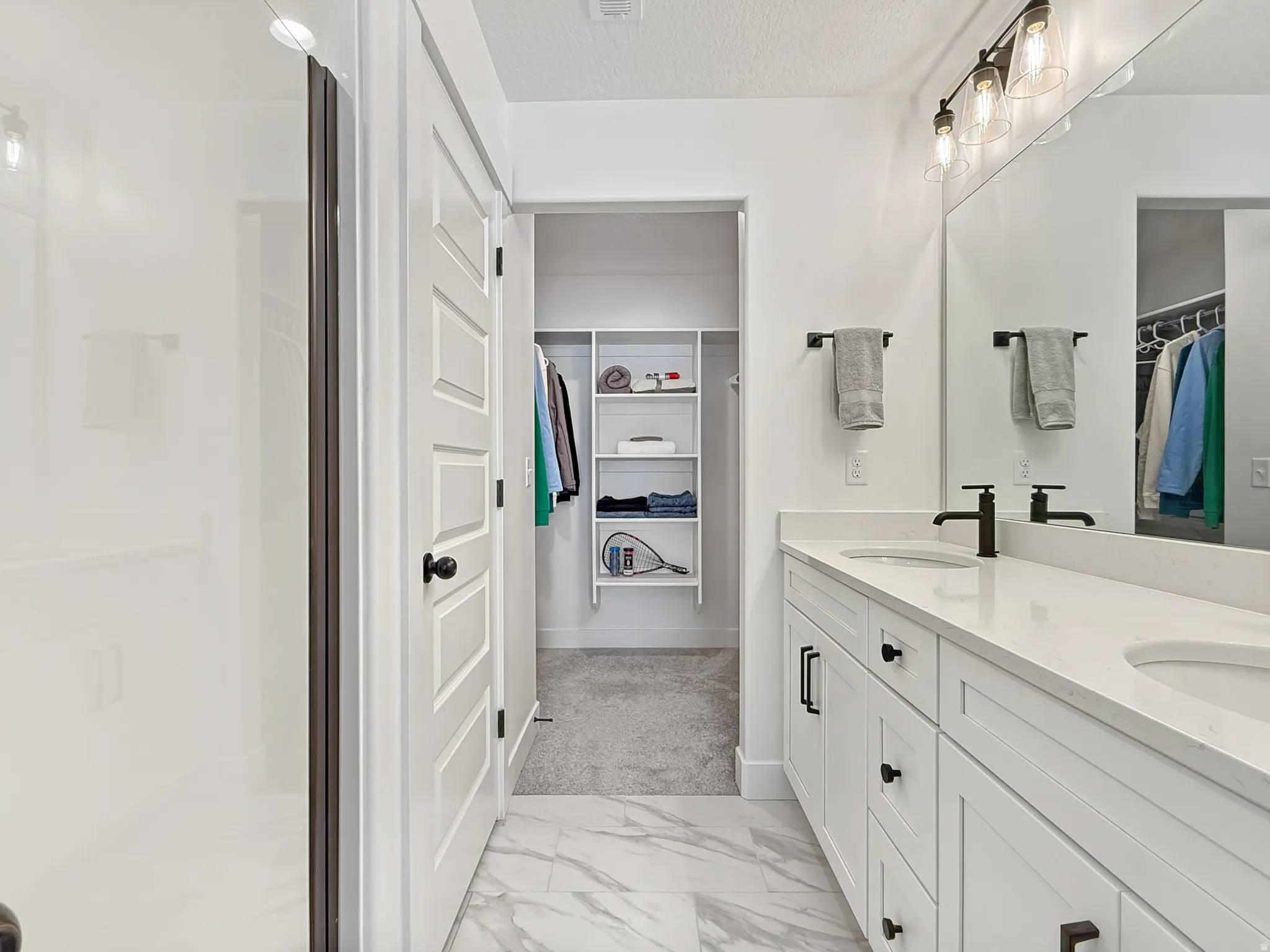 Full bathroom featuring a spacious closet, double vanity, light marble finish flooring, a textured ceiling, and a shower stall