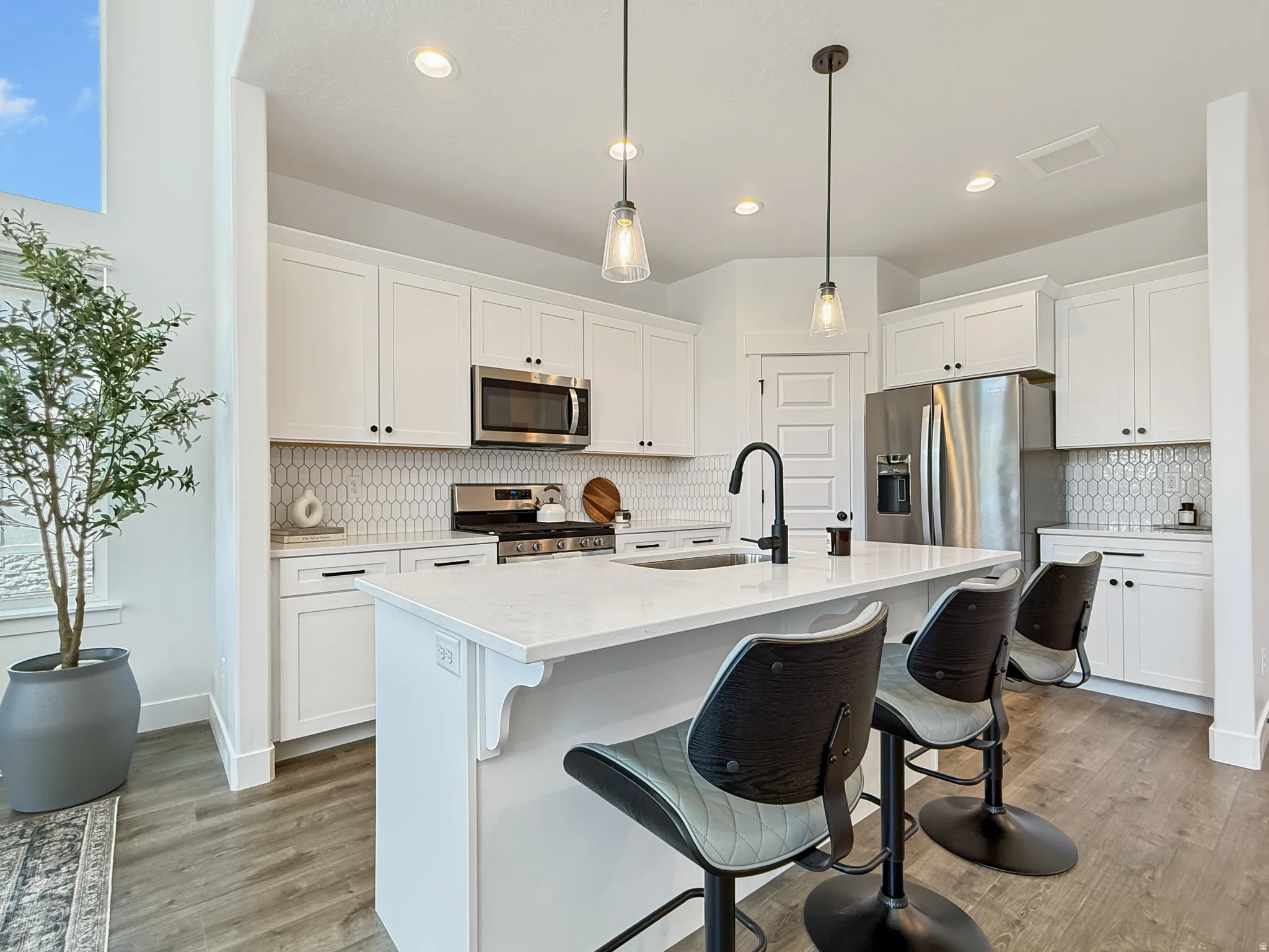 Kitchen featuring tasteful backsplash, stainless steel appliances, white cabinets, and a kitchen breakfast bar