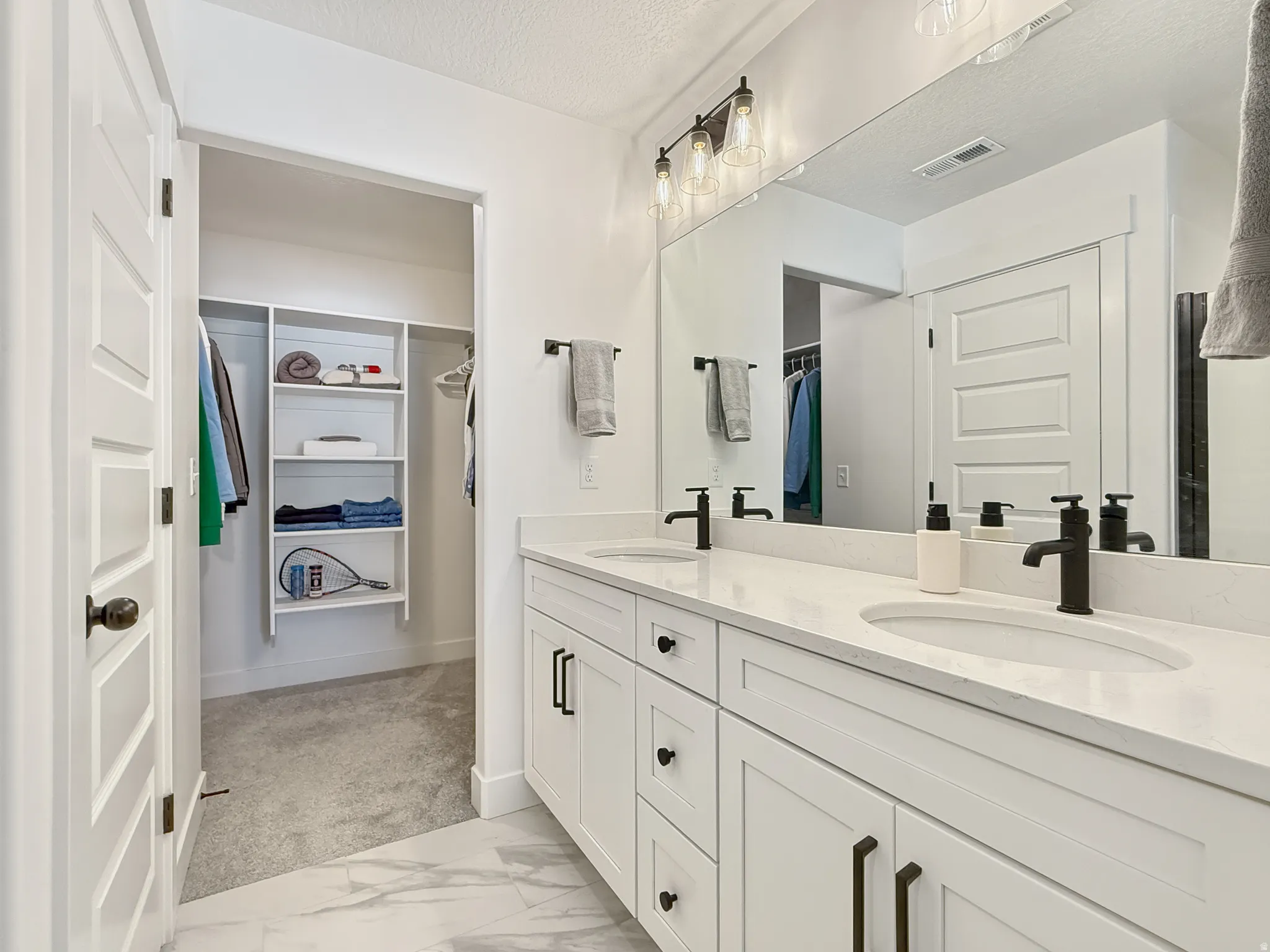 Full bathroom with a walk in closet, double vanity, and a textured ceiling
