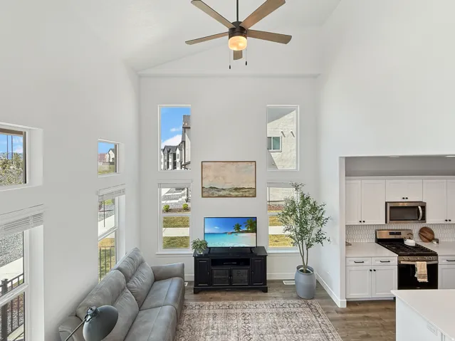 Living area with a ceiling fan, light wood finished floors, plenty of natural light, and vaulted ceiling