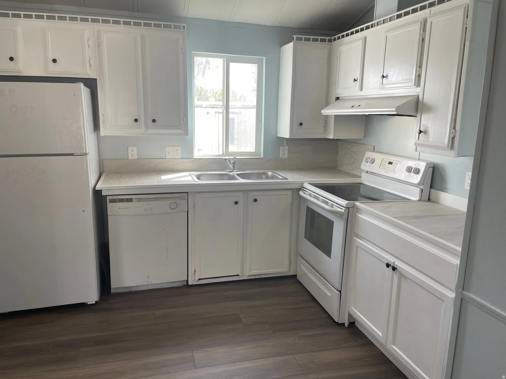Kitchen featuring white cabinets, white appliances, light countertops, and dark wood finished floors