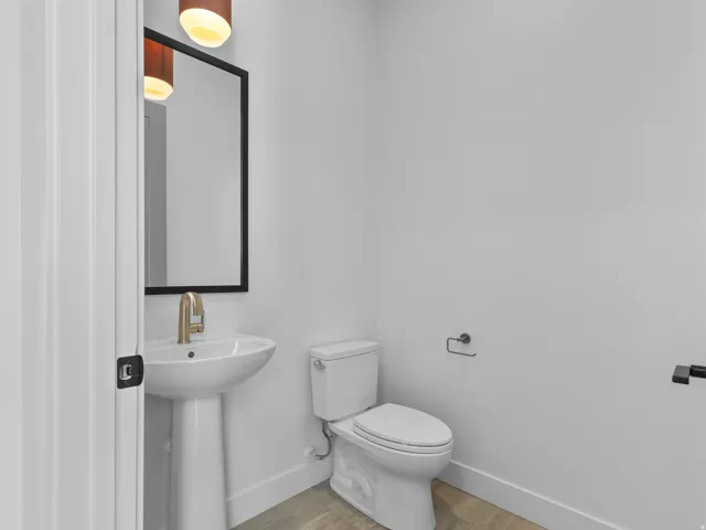Pedestal sink with brass-finish faucet, rectangular mirror with black frame, and white toilet