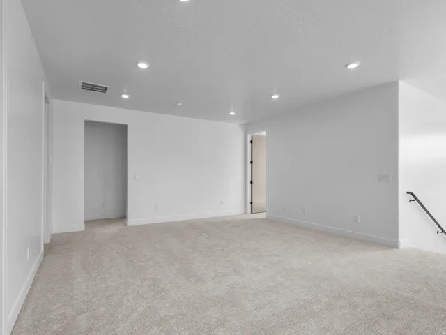 Spacious room featuring neutral carpeting, recessed ceiling lighting, and crisp white walls