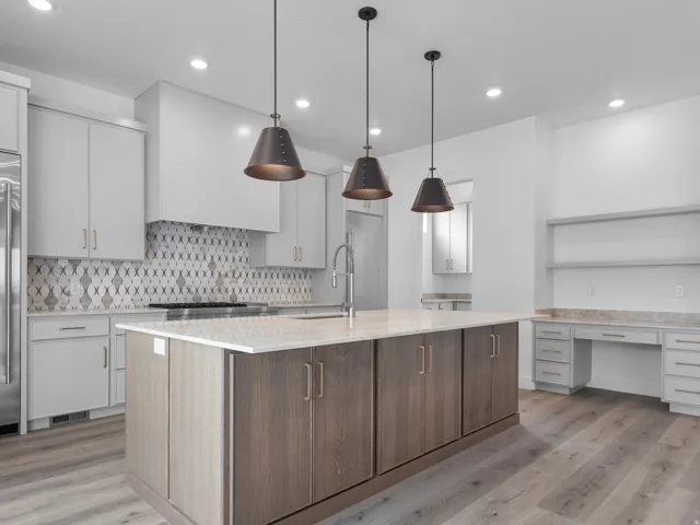 Spacious kitchen featuring a large central island with light-toned countertop, wood-finish flooring, recessed lighting, pendant light fixtures, and built-in desk cabinetry