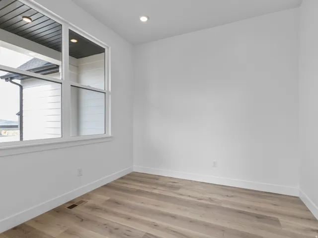 Bright room featuring a large window, recessed lighting, white walls, and wood-finish flooring