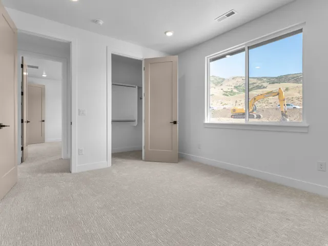 Bright room featuring a large window, neutral carpeting, and a closet with built-in shelving