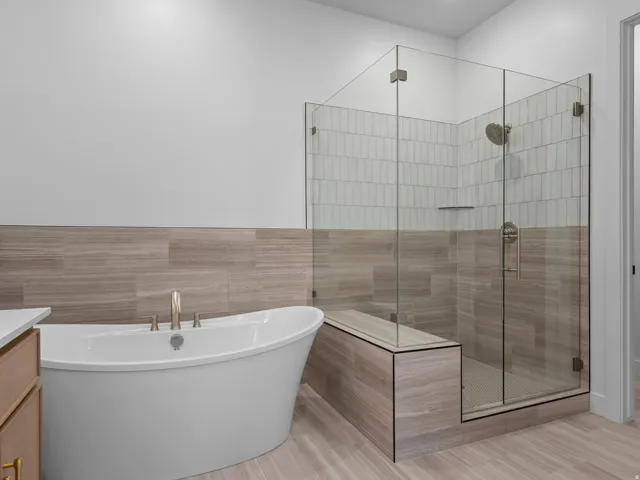 Freestanding soaking tub featuring brushed gold fixtures alongside a glass-enclosed shower with a built-in bench