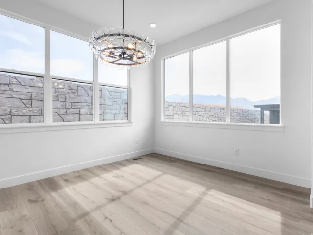 Bright interior featuring a contemporary chandelier, multiple large windows, light wood-finish flooring, white walls, and white baseboards