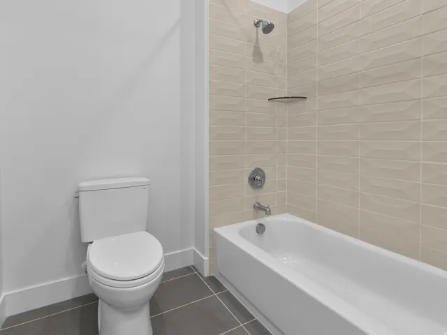 Bathtub and shower combination featuring beige textured tile surround