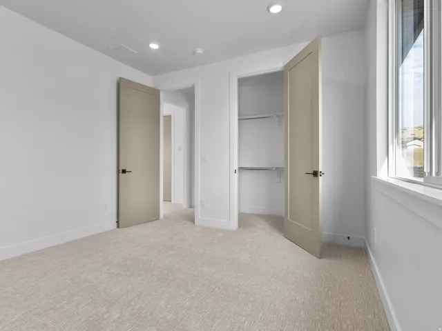 Neutral-toned bedroom featuring plush carpet flooring, recessed lighting, and a window with white trim
