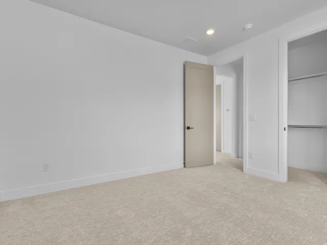 Spacious bedroom featuring neutral wall finishes, neutral-tone carpet flooring, recessed ceiling lighting, and multiple closet doors providing ample storage