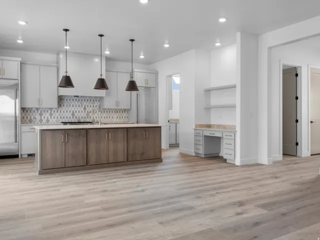 Spacious kitchen featuring a large island with wood-finish cabinetry, a patterned tile backsplash, stainless steel appliances, and ceiling-mounted pendant lighting