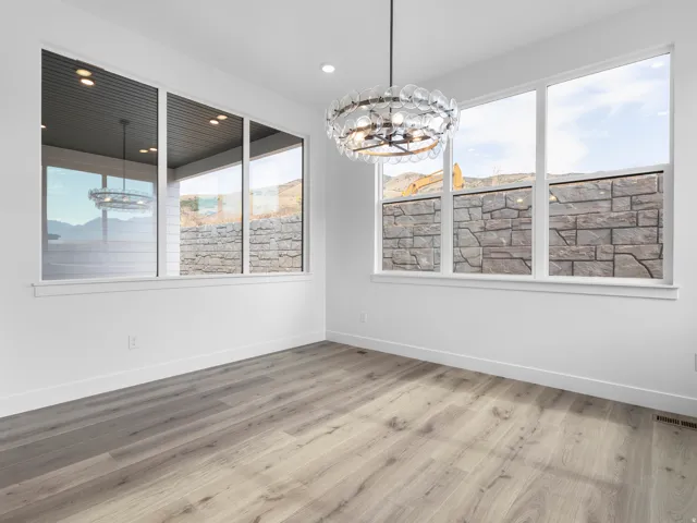 Spacious room featuring large white-framed windows, wood-finish flooring, a contemporary chandelier, recessed ceiling lighting, and crisp white walls