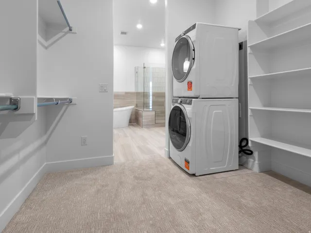 Integrated laundry area with stacked appliances, alongside built-in shelving, carpeted flooring, and a wardrobe hanging rod