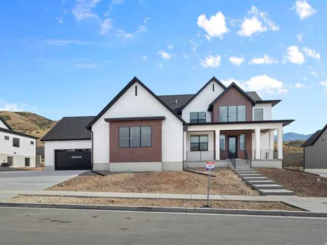 Modern farmhouse architecture featuring a white exterior with brick accents, prominent gables, a covered front porch, and an attached two-car garage